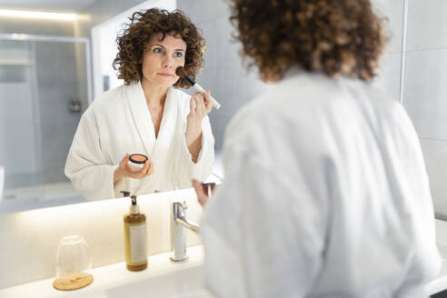 Beautiful woman applying powder from make-up brush in bathroom - JPTF00728