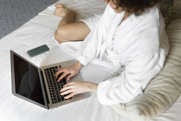 Mature businesswoman in bathrobe working on laptop in hotel room - JPTF00729