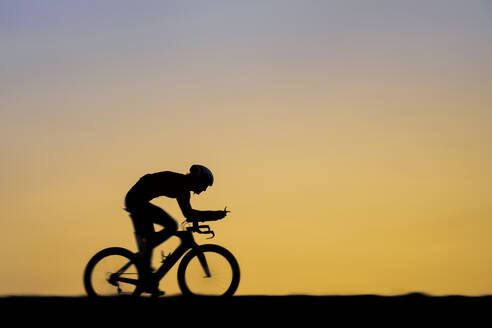 Männlicher Triathlet fährt bei Sonnenuntergang Fahrrad - STSF02893