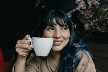 Lächelnde Frau träumt, während sie eine Kaffeetasse hält - DSIF00387