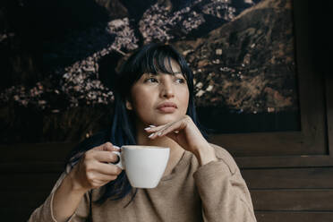 Frau mit Hand am Kinn, die einen Kaffee hält und wegschaut - DSIF00388