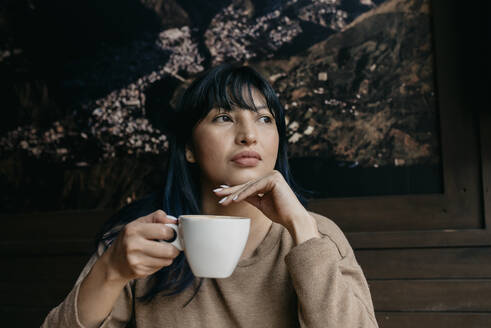 Frau mit Hand am Kinn, die einen Kaffee hält und wegschaut - DSIF00388