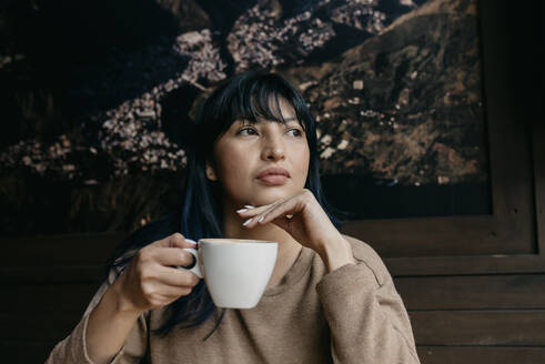 Woman with hand on chin holding coffee while looking away - DSIF00388