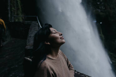 Frau mit geschlossenen Augen entspannt am Wasserfall - DSIF00395