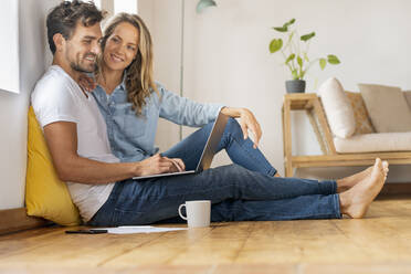 Mid adult man using laptop while sitting with girlfriend at home office - SBOF03669