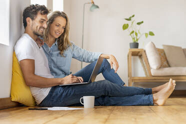 Relaxed couple looking at laptop while sitting together at home office - SBOF03671