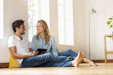 Mann mit digitalem Tablet sieht seine Freundin an, während er zu Hause auf dem Boden sitzt - SBOF03682