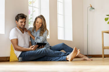 Smiling couple using digital tablet while sitting on floor at home - SBOF03683