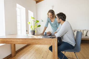 Mann diskutiert mit Freundin bei der Arbeit am Laptop im Home Office - SBOF03686