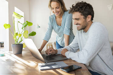 Fröhliches Paar bei der Arbeit am Laptop im Home Office - SBOF03688