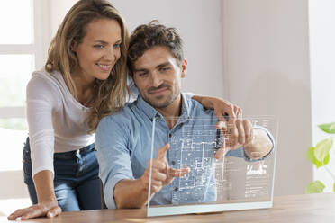 Mid adult couple looking at floor plan over transparent screen at home - SBOF03696
