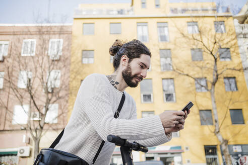 Hipster-Mann benutzt Mobiltelefon auf einem Tretroller - EBBF03002
