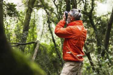 Älterer männlicher Forscher beim Fotografieren mit der Kamera im Wald am Wochenende - PNAF01322