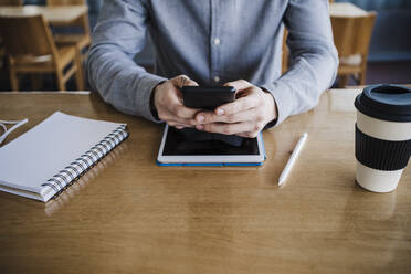Businessman using smart phone over digital tablet on desk at work place - EBBF03034