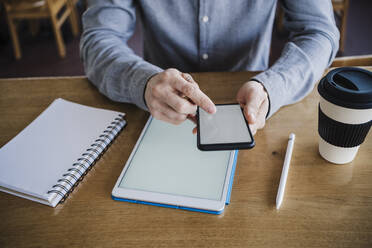 Male businessperson working on mobile phone and digital tablet at work place - EBBF03035