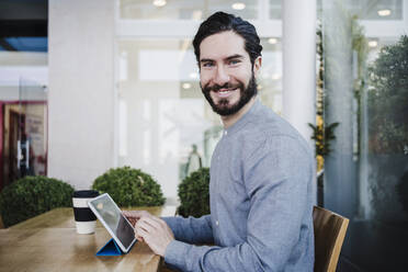 Smiling businessman with digital tablet on desk at work place - EBBF03043