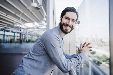 Happy mid adult male entrepreneur leaning on railing at work place balcony - EBBF03052