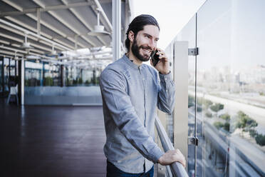 Kreativer Geschäftsmann, der mit seinem Handy telefoniert und durch ein Glas im Büro schaut - EBBF03054