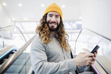 Lächelnder Mann mit Mobiltelefon auf der Rolltreppe - EBBF03060