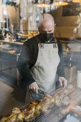 Männlicher Koch schneidet Brathähnchen durch Glas in einer Restaurantküche - EGAF02216