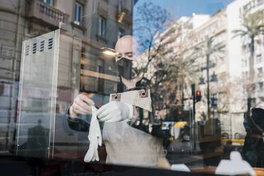 Mann mit Schutzhandschuhen durch Glas in Restaurant gesehen - EGAF02219