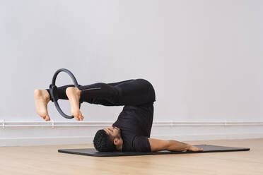 Mann, der mit einem Pilates-Ring an der Wand im Fitnessraum trainiert - AODF00432