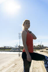 Young female athlete standing on pier during sunny day - AMPF00157