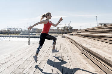 Weibliche Joggerin bei Aufwärmübungen auf Stufen an einem sonnigen Tag - AMPF00159