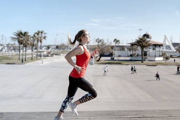 Female jogger running on pier during sunny day - AMPF00163