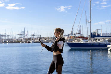 Young woman taking selfie through smart phone while standing at harbor - AMPF00172