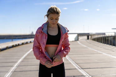 Female jogger wearing jacket while standing on boardwalk - AMPF00185