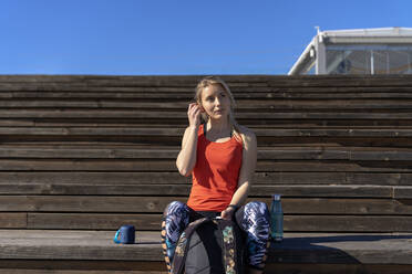 Nachdenkliche Sportlerin auf dem Pier sitzend an einem sonnigen Tag - AMPF00199