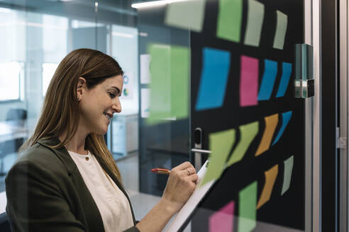 Unternehmerin bei der Planung von Strategien, während sie mit einem Klebezettel an einer Glaswand im Büro steht - XLGF01417