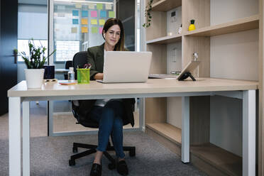 Konzentrierte Unternehmerin arbeitet am Laptop, während sie am Schreibtisch im Büro sitzt - XLGF01437