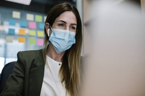Female entrepreneur with protective face mask working at office during COVID-19 - XLGF01440