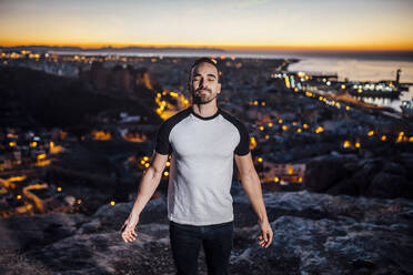 Man with eyes closed standing on rock during sunrise - MIMFF00644