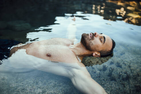 Man with eyes closed lying on water during vacations - MIMFF00667