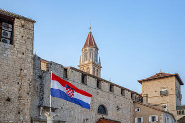 Kroatien, Gespanschaft Split-Dalmatien, Trogir, kroatische Flagge vor alten Stadthäusern mit Glockenturm der Kirche des Heiligen Nikolaus im Hintergrund - MAMF01696