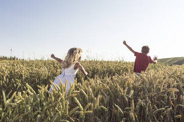 Girl and boy running through agricultural field during sunset - WFF00514