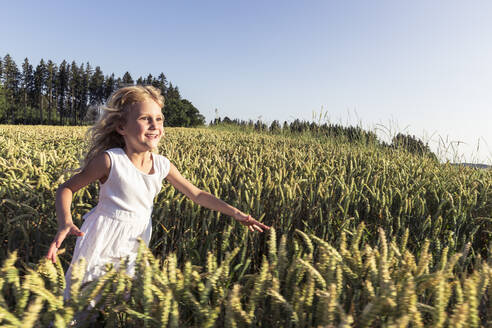 Cheerful girl running amidst crops plants during sunset - WFF00516