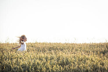 Mädchen mit zerzaustem Haar läuft bei Sonnenuntergang durch ein landwirtschaftliches Feld - WFF00521