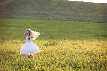Girl with arms outstretched spinning on green grass during sunset - WFF00527