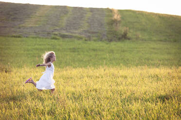 Girl with arms outstretched running in meadow during sunset - WFF00528