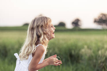 Laughing girl with blond hair holding leaf while looking away - WFF00537