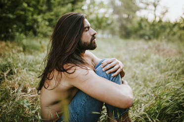 Side view of young female with bare breasts wearing casual jeans