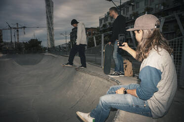 Männlicher Skateboarder fährt Schlittschuh, während ein Freund im Park mit seinem Smartphone fotografiert - MASF22523