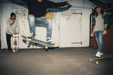 Männlicher Skater mit Skateboard, der von Freunden auf der Straße gesprungen wird - MASF22531