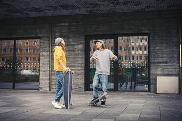 Male friends talking while standing with skateboard on footpath - MASF22561