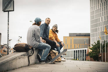 Männliche Freunde, die auf einer Mauer sitzend miteinander reden - MASF22562