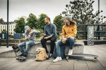 Lächelnde männliche Freunde sitzen über einer Stützmauer auf einem Fußweg - MASF22563
